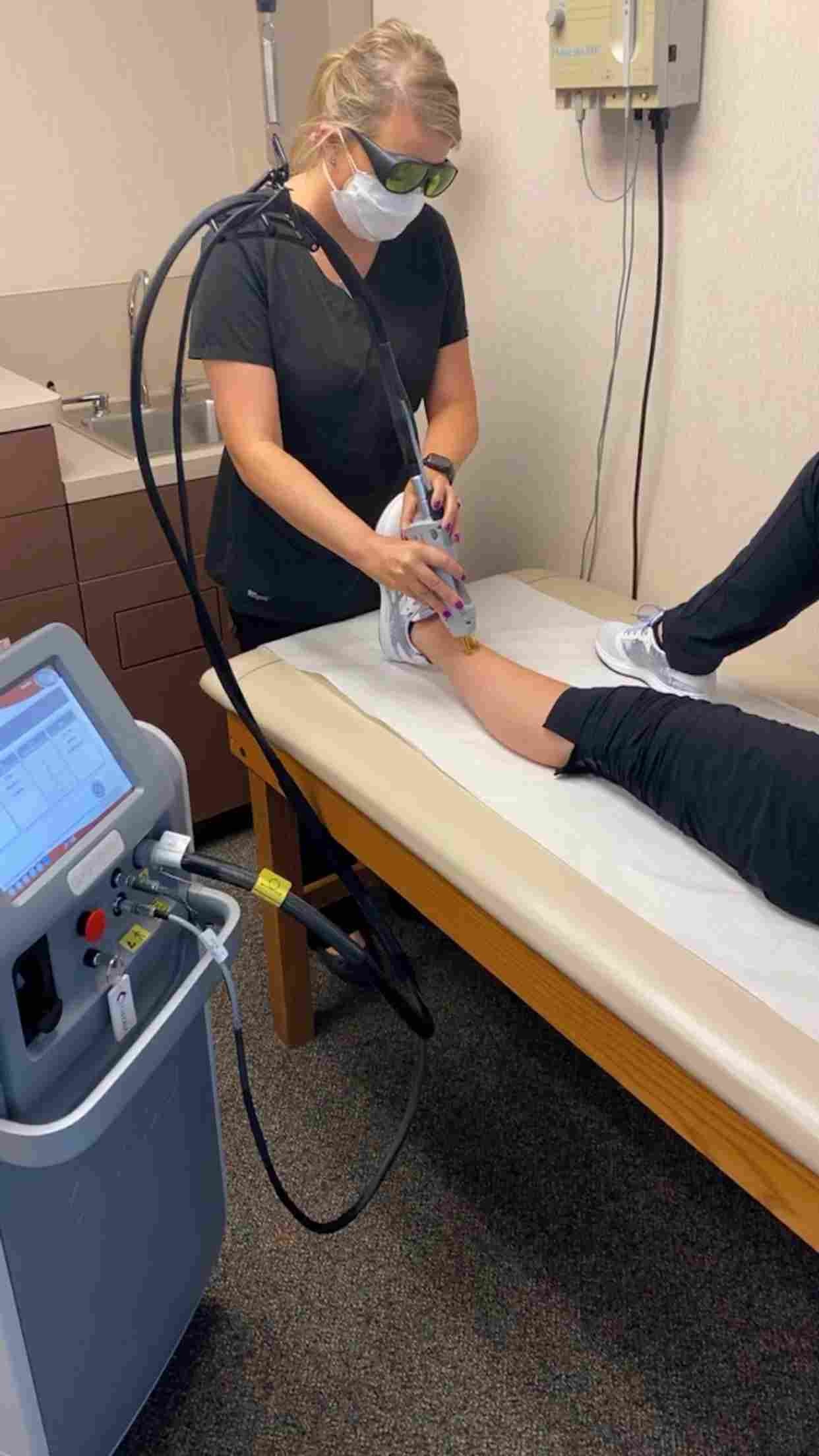 A person doing a laser leg treatment on a patient