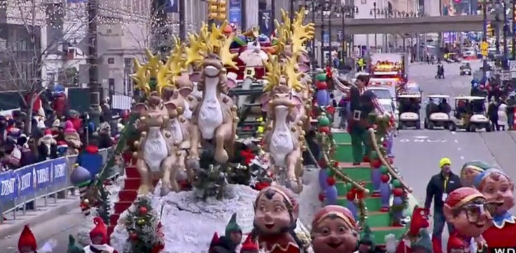 A Christmas parade in a busy street with cars