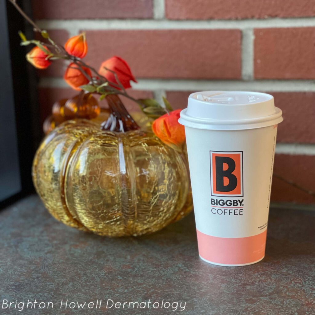 A cup of biggby coffee next to a glass pumpkin